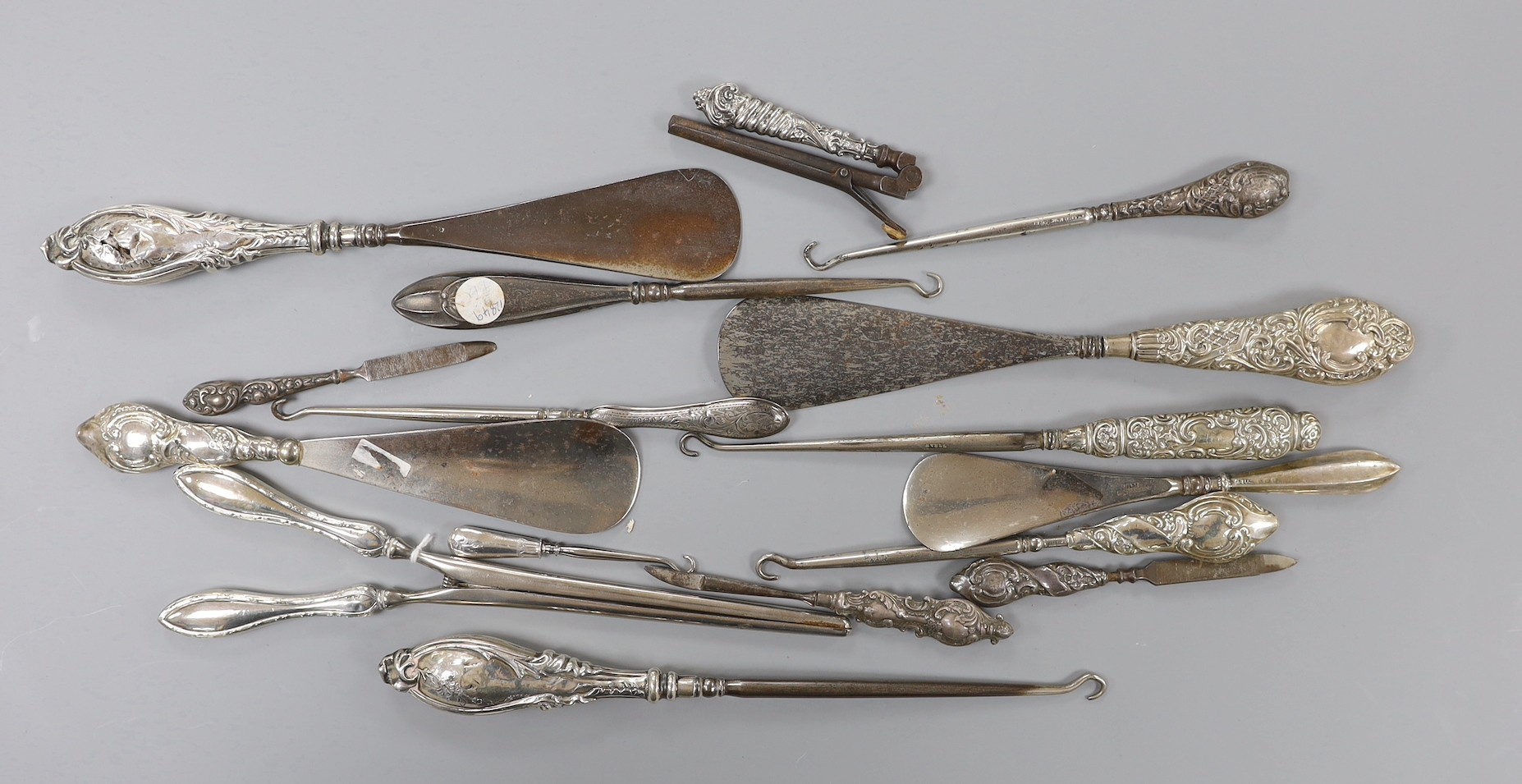 Four repousse silver handled shoe horns, seven similar button hooks, three nail implements, a pair glove stretchers and small pair of curling tongs.